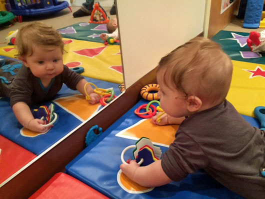An infant on the floor looking in at his toys in a mirror