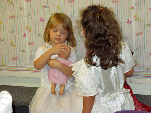 Two pre-Kinders dressed up and playing in the dramatic play area with a baby doll.