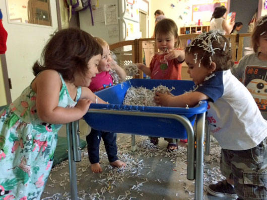 Five preschoolers playing at a water table filled with shredded newspaper