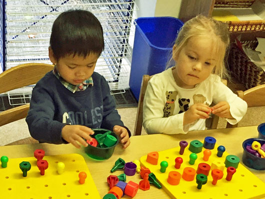 Parallel play of two preschool children at a table with peg shapes and boards