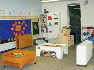 View of classroom with Lego center, dramatic play area, bulletin boards and reading center